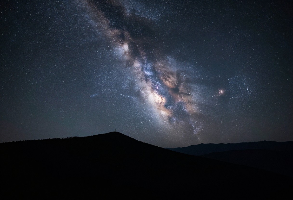 A wide-field photograph of the Milky Way galaxy rising over a silhouetted mountain landscape