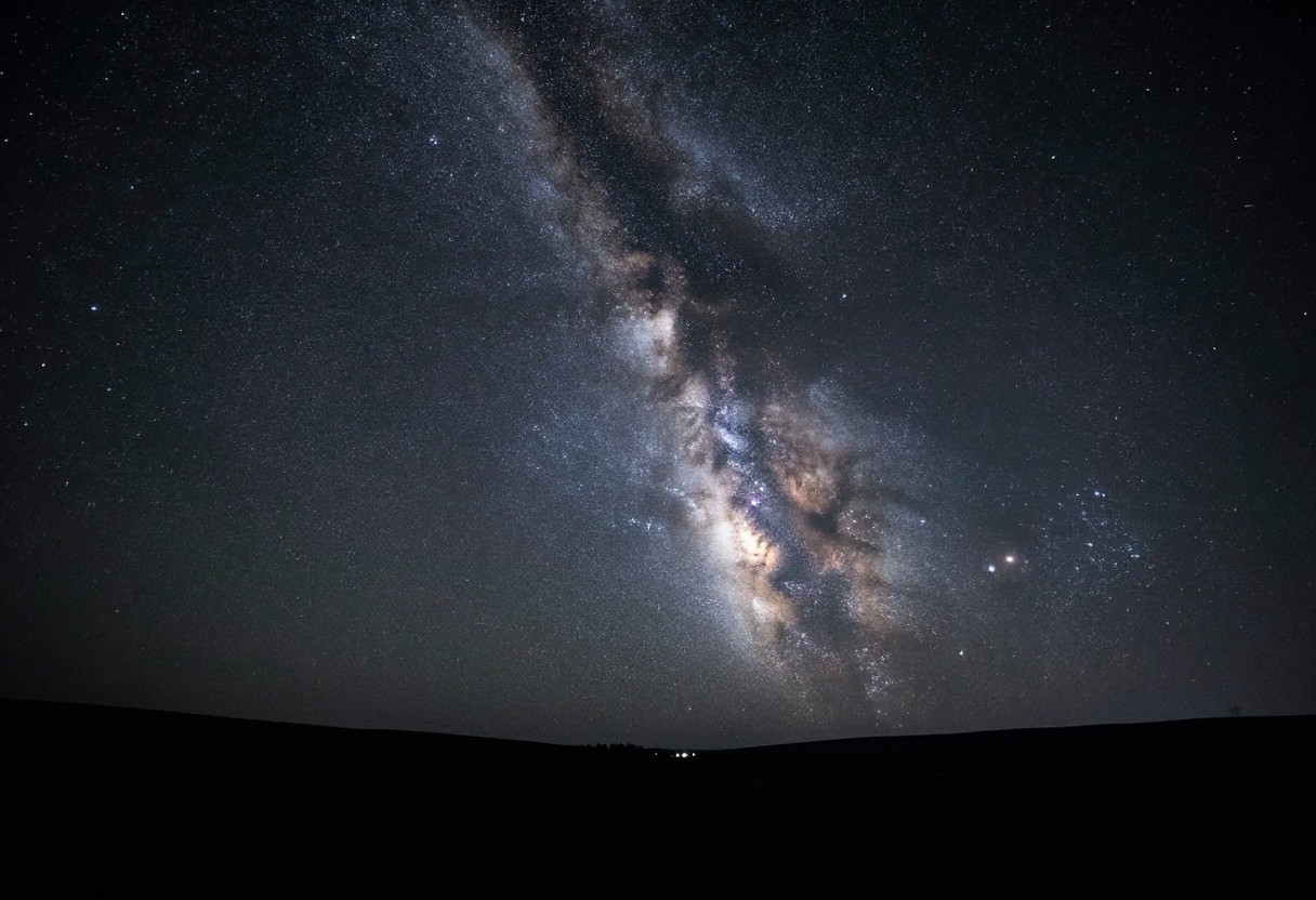 A brilliant starry night sky with the Milky Way band clearly visible arching overhead above a dark landscape